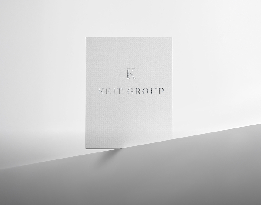 Minimalist white card standing upright with embossed text 'KRIT GROUP' and letter 'K' above it on a clean white and gray background.