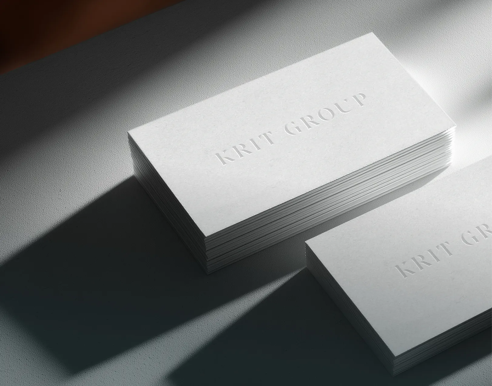Due pile di biglietti da visita bianchi con la scritta in rilievo 'KRIT GROUP' su una superficie illuminata da luce naturale.