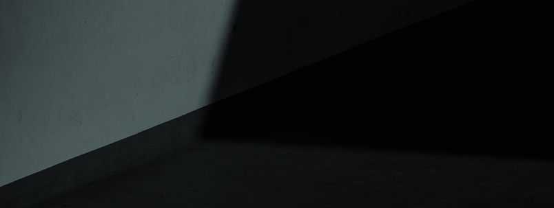 Angolo di una stanza scarsamente illuminata con muro grigio e pavimento scuro.